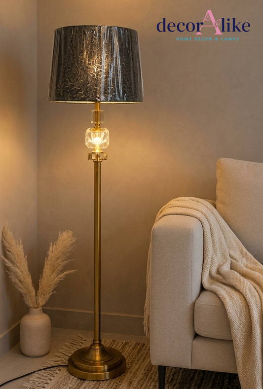 Gold brass crystal accent floor lamp with pleated charcoal shade beside a grey throw