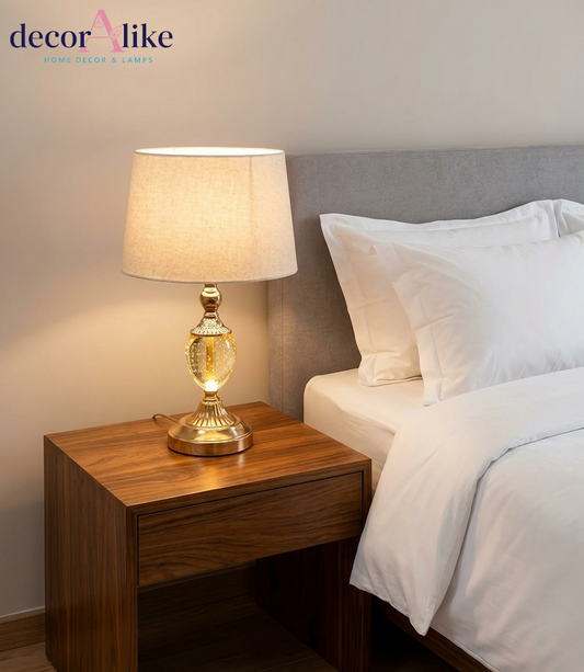 Gold table lamp with clear seeded-glass body and beige fabric shade on a wooden table
