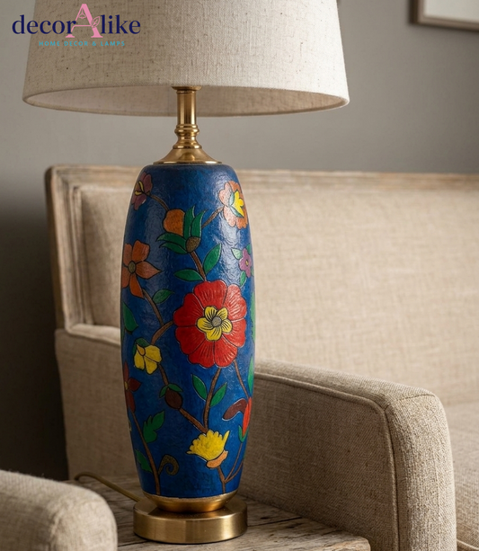 Blue hand-painted floral Camel skin table lamp with brass base and cream linen drum shade on a rustic wooden table
