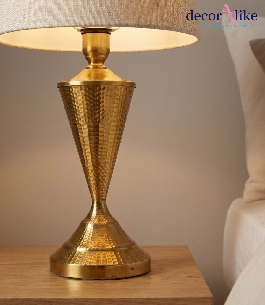Hammered brass table lamp with hourglass base and natural linen shade on an oak bedside table