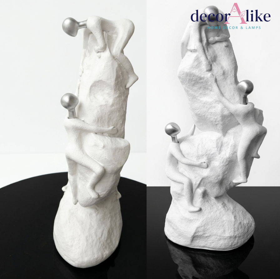 Surreal white figures climbing textured rock sculpture with silver spheres – Decoralike Lahore
