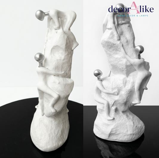 Surreal white figures climbing textured rock sculpture with silver spheres – Decoralike Lahore