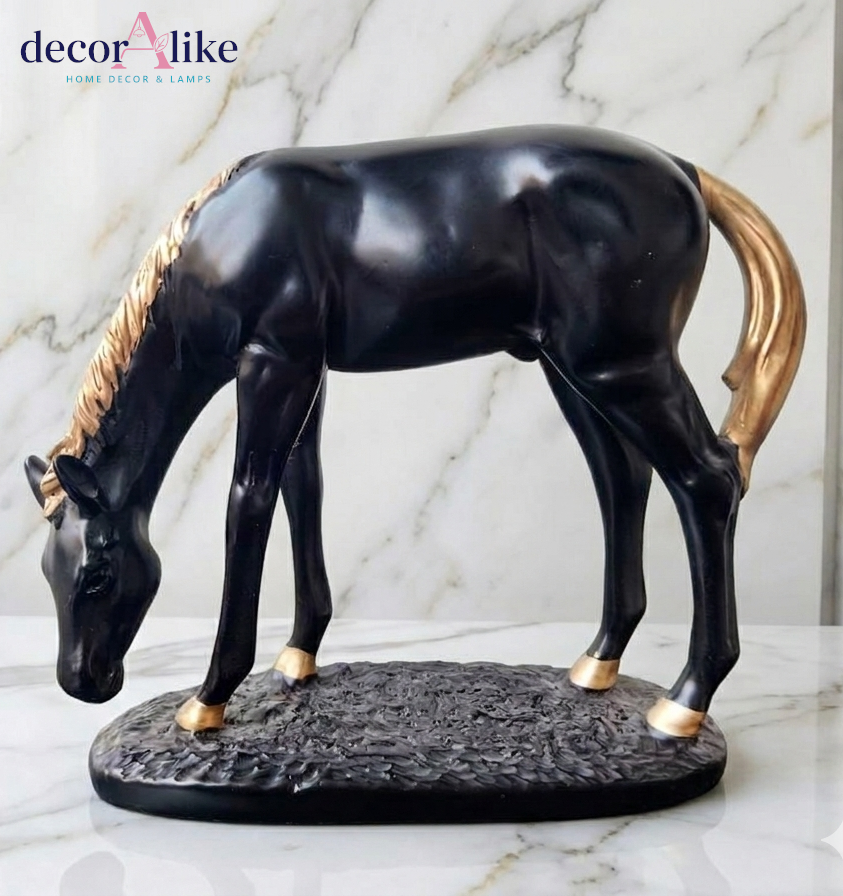 A glossy black horse figurine with gold-colored mane, tail, and hooves, standing on a textured dark base against a white marble background. A 'decorAlike' brand logo is visible in the top left corner.