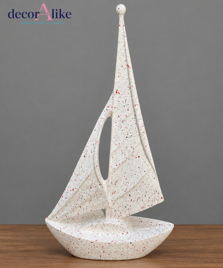 A decorative sailboat sculpture with a textured, speckled off-white finish, displayed on a wooden surface against a solid gray background. The brand logo 'decorAlike' is visible in the top left corner.