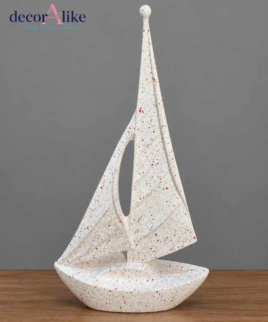 A decorative sailboat sculpture with a textured, speckled off-white finish, displayed on a wooden surface against a solid gray background. The brand logo 'decorAlike' is visible in the top left corner.