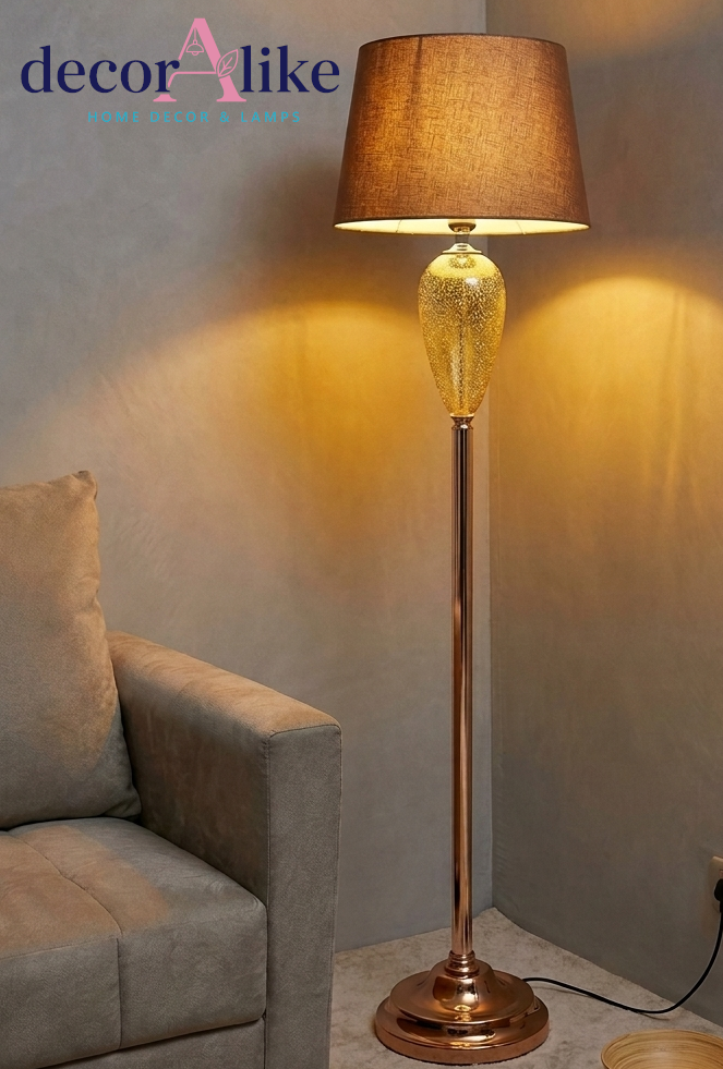 Rose gold floor lamp with speckled amber glass base 
and mocha linen shade glowing warmly in living room corner