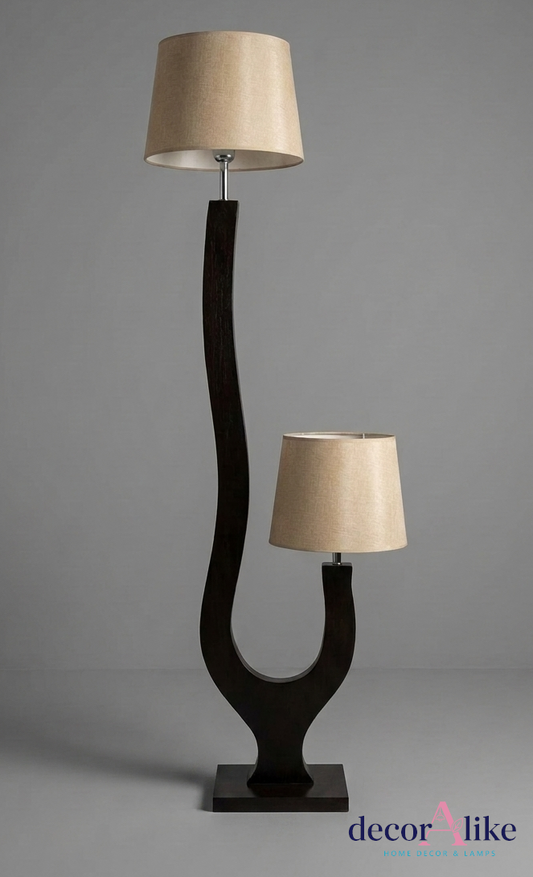 A modern two-light floor lamp with a dark curved wooden base and two beige fabric drum shades, photographed against a neutral gray studio background.