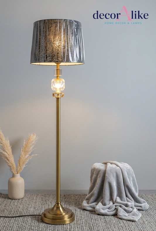 Gold brass crystal accent floor lamp with pleated charcoal shade beside a grey throw