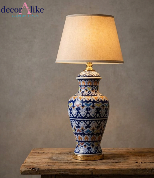 Blue floral ceramic table lamp with multicolour motifs, gold accents and beige fabric shade on a wooden table