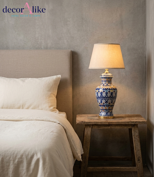 Blue floral ceramic table lamp with multicolour motifs, gold accents and beige fabric shade on a wooden table