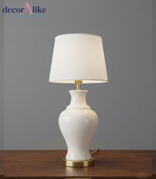 White ceramic vase table lamp with gold base and cream fabric shade on a wooden table