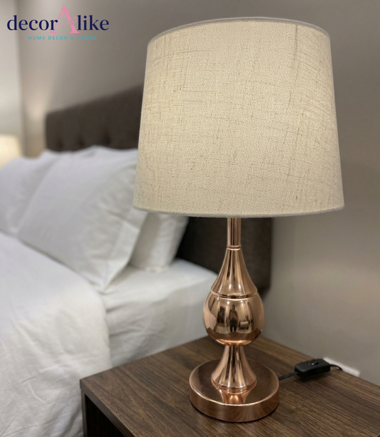 Modern rose gold table lamp with beige linen shade on wooden side table — bedside lamp Pakistan