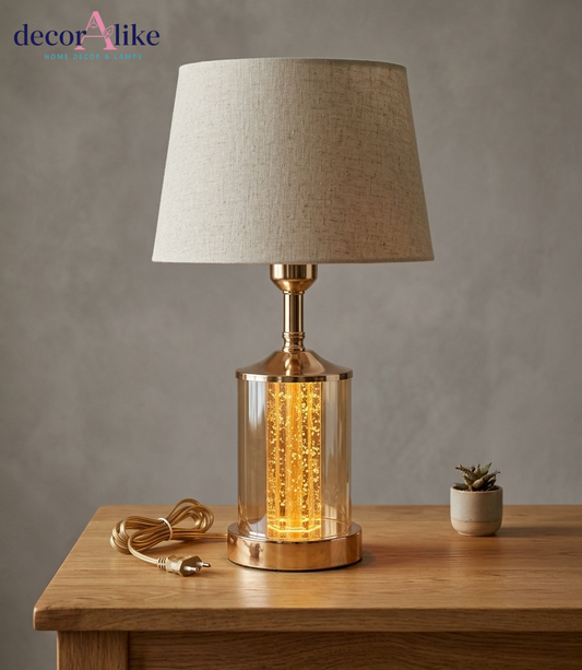Modern gold bubble glass table lamp with glowing filament effect and beige linen shade on wooden table - DecorAlike Pakistan