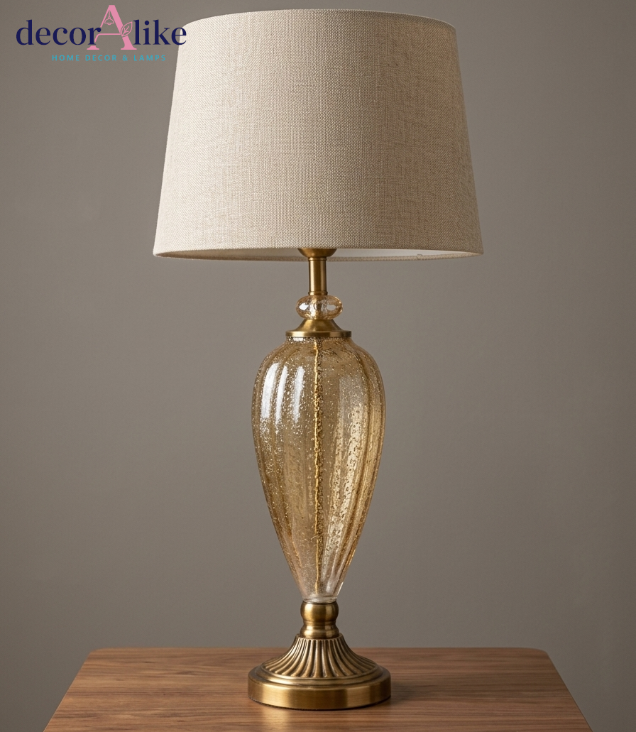 Tall gold seeded glass urn table lamp with fluted brass pedestal base and beige linen drum shade on a wooden console