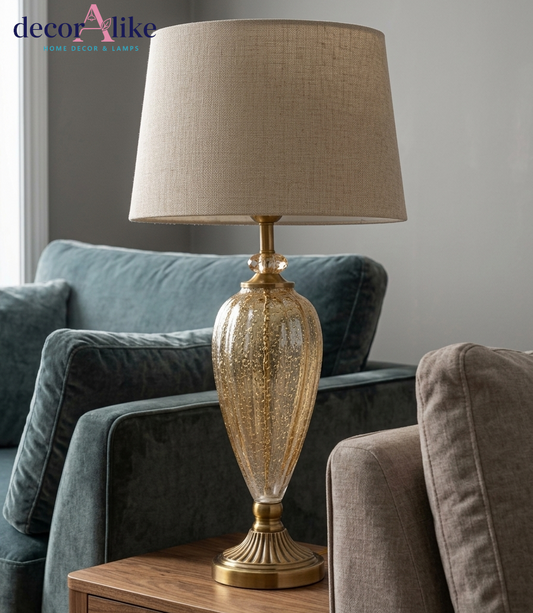 Tall gold seeded glass urn table lamp with fluted brass pedestal base and beige linen drum shade on a wooden console