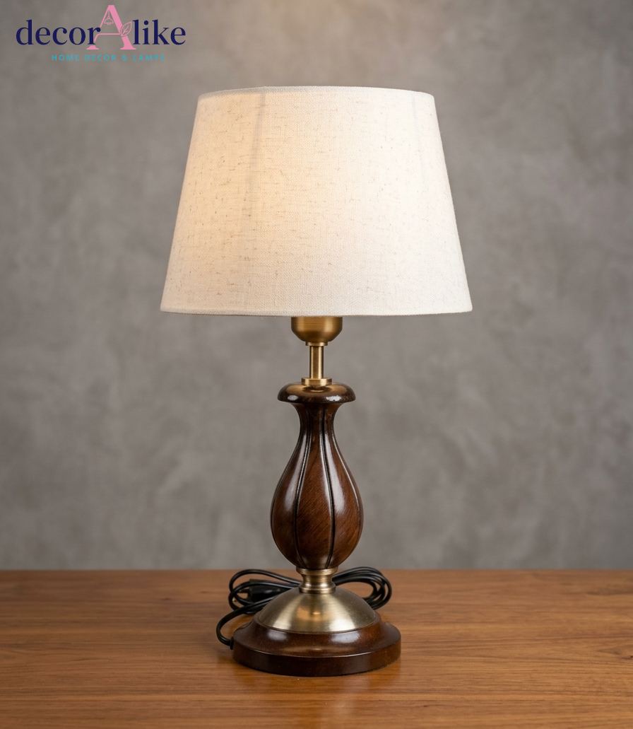 Carved wooden table lamp in walnut finish with brass accents and ivory linen shade on a wooden side table