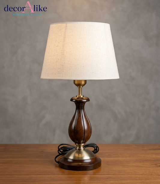 Carved wooden table lamp in walnut finish with brass accents and ivory linen shade on a wooden side table