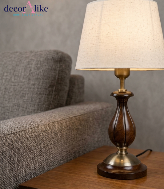 Carved wooden table lamp in walnut finish with brass accents and ivory linen shade on a wooden side table