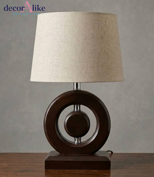 Modern walnut-finish wooden ring table lamp with chrome accents and beige linen drum shade on a wooden table