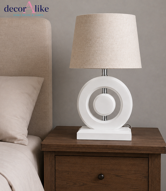 Modern white-finish wooden ring table lamp with chrome accents and beige linen drum shade on a wooden table