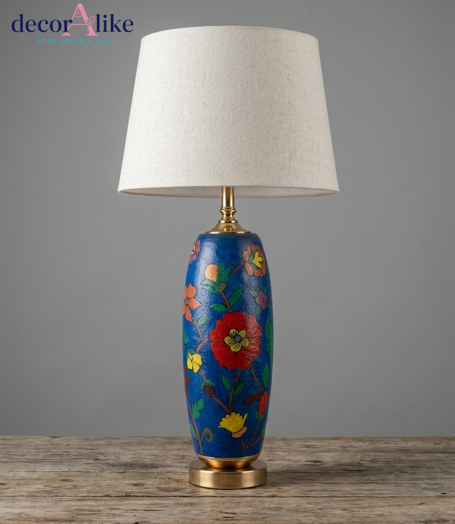 Blue hand-painted floral Camel skin table lamp with brass base and cream linen drum shade on a rustic wooden table