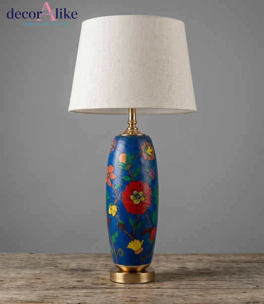 Blue hand-painted floral Camel skin table lamp with brass base and cream linen drum shade on a rustic wooden table
