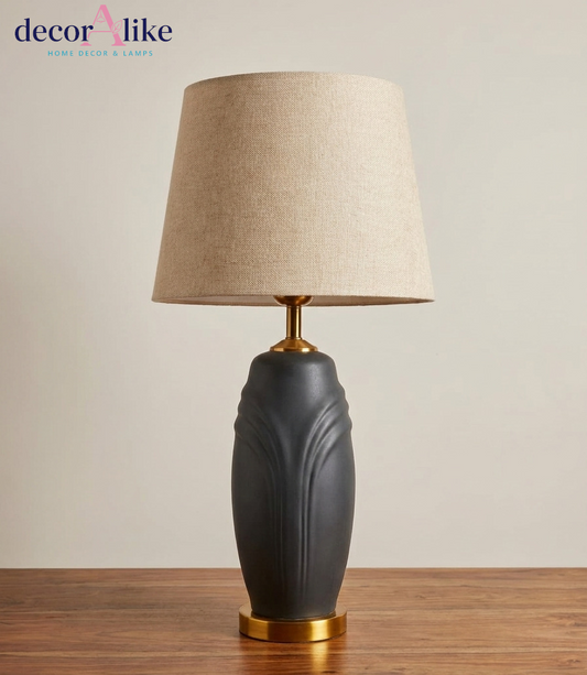 Matte charcoal ceramic table lamp with sculpted leaf relief, brass base and beige linen drum shade on a wooden table