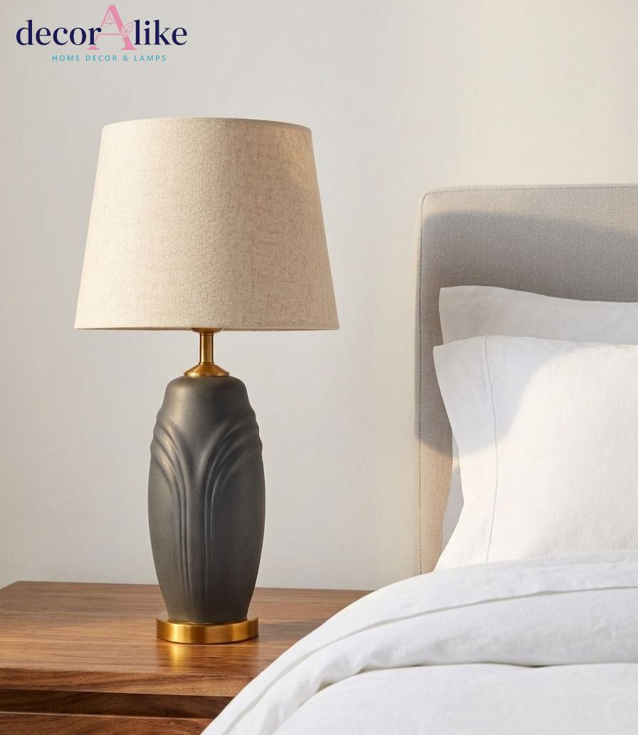 Matte charcoal ceramic table lamp with sculpted leaf relief, brass base and beige linen drum shade on a wooden table