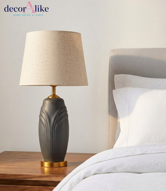 Matte charcoal ceramic table lamp with sculpted leaf relief, brass base and beige linen drum shade on a wooden table