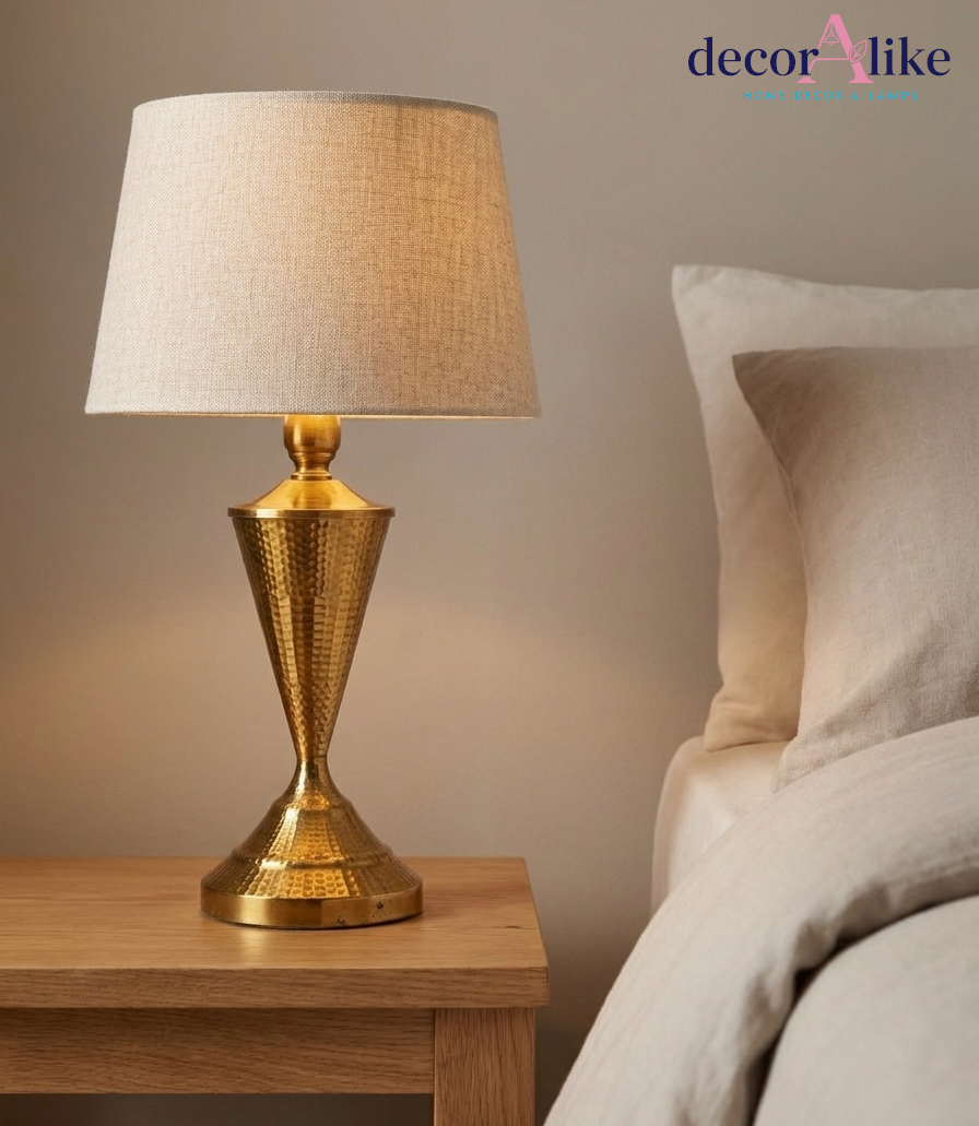 Hammered brass table lamp with hourglass base and natural linen shade on an oak bedside table