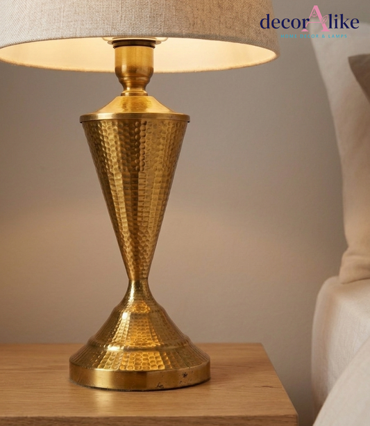Hammered brass table lamp with hourglass base and natural linen shade on an oak bedside table