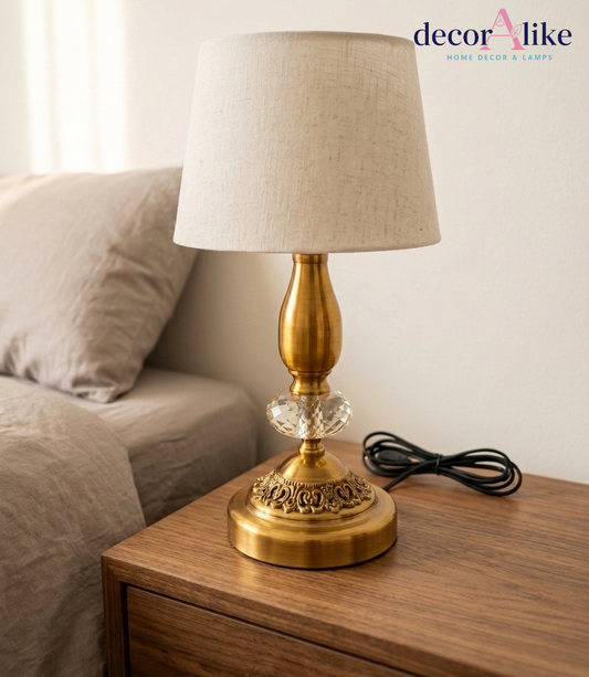 Antique brass table lamp with crystal accent and beige linen shade on wooden nightstand — Decoralike Pakistan
