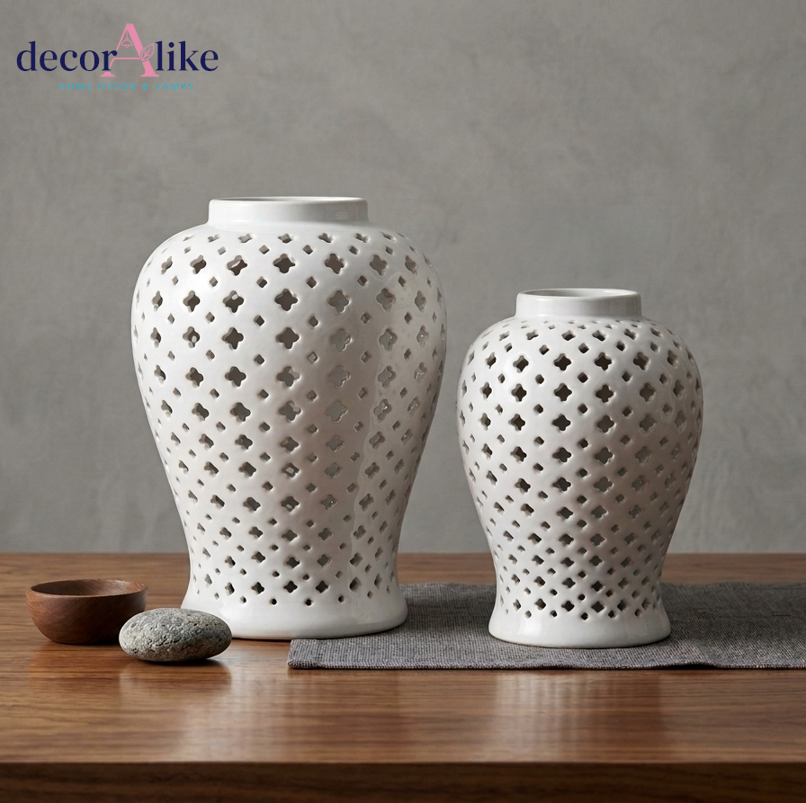 Two white ceramic decorative vases with geometric l cutouts, displayed on a wooden surface against a textured gray wall. Shop now at decoralike