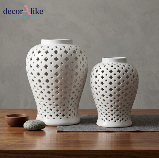 Two white ceramic decorative vases with geometric l cutouts, displayed on a wooden surface against a textured gray wall. Shop now at decoralike
