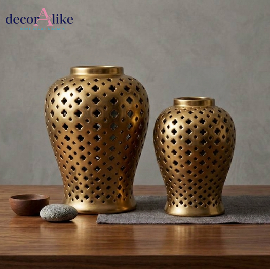 Two golden ceramic decorative vases with geometric l cutouts, displayed on a wooden surface against a textured gray wall. Shop now at decoralike